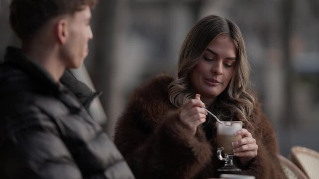A young couple enjoys coffee at an outdoor in Paris France The woman stirs her latte with a spoon The clip captures a romantic date in a Parisian setting Slow motion.