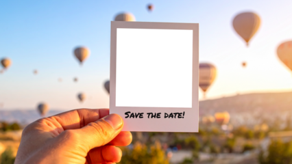 Hand holding an instant photo with 'Save the Date' message. The background shows a stunning sunrise landscape with many hot air balloons flying, creating a romantic and adventurous travel scene.