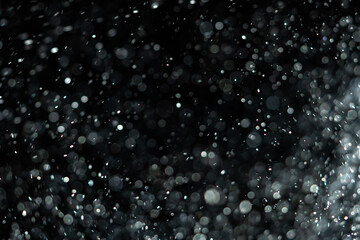 Tiny dust particles fly randomly in the smoky air, an empty template of space for objects. Many glittering particles of powder fall onto an empty black contrasting background in the rays of light.