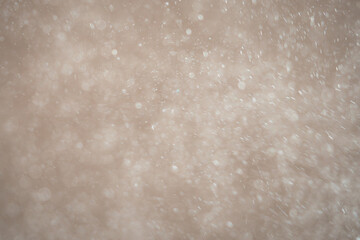 White particles or snowflakes falling diagonally on a light soft background with a motion blur effect.