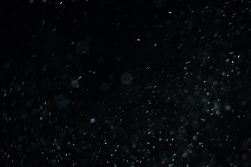 Soaring little pieces of dust floating in a ray of light on a black background. Twirling randomly...