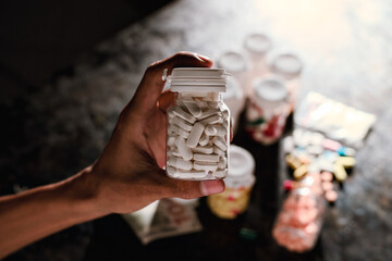 A person's hand firmly grips a clear plastic prescription bottle densely packed with white, oblong tablets.