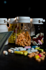 A dramatic low-key photograph captures multiple prescription pill bottles filled with assorted capsules and tablets, symbolizing prescription costs, healthcare, and pharmaceutical industry concepts.