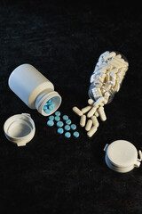 Close-up view of blue round tablets and white oblong capsules scattered after spilling from white and clear plastic medicine bottles. Health, treatment options, and prescription dosage management