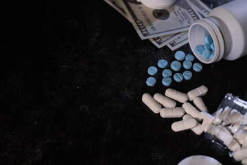 Prescription drugs, white capsules and blue tablets, are shown spilled near US currency, pharmaceutical dependence, or the illegal drug trade's financial aspects.
