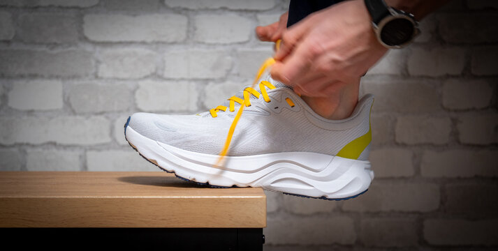 Close-up of an athlete tying yellow laces on a modern white running shoe. This high-angle shot highlights preparation, fitness routine, and sports gear against a clean, urban background.