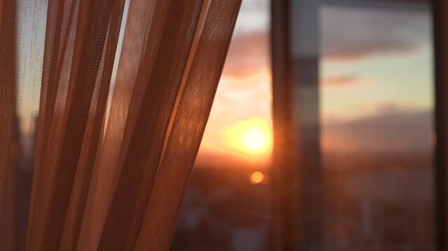 Golden hour sunset shining through sheer window curtain, with warm light filling room and creating serene and peaceful atmosphere. Pull back curtain from window at home for light at sunrise.