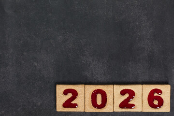New Year 2026. Square cookies with red marmalade filling in the shape of the numbers 2026. Dark gray background. Top view. Copy space