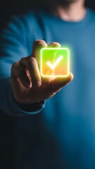 A person s hand holding a glowing illuminated square button with a vibrant green checkmark symbol