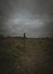 Lonely man in a hoodie standing on a meadow under a dramatic cloudy sky, moody atmosphere, solitude concept.