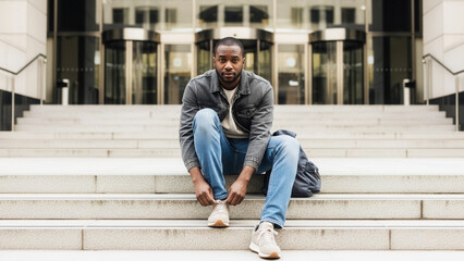 African-American man tying shoelaces on steps, casual fashion and urban lifestyle in city setting