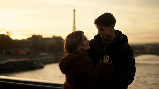A young couple embraces on a bridge in Paris France with the Eiffel Tower visible in the background during a golden sunset The lovers are hugging on a bridge over the Seine river enjoying a romantic m