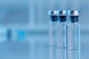 Vaccine in glass vials on mirror surface against blurred grey background, closeup. Space for text