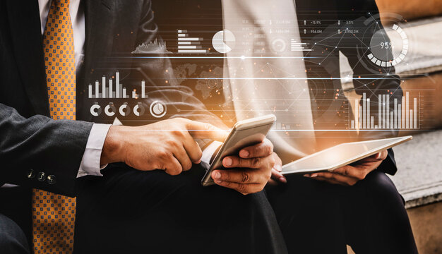 Two business professionals engage with mobile devices while analyzing digital data and charts, representing teamwork and modern technology in an office setting. Scalp - Powered by Adobe