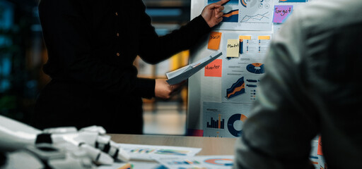 A dynamic business meeting scene showcasing team members presenting charts and graphs in a modern office, highlighting collaboration and strategic planning.Noogenesis