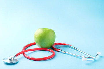 Ripe apple and stethoscope on light blue background, closeup