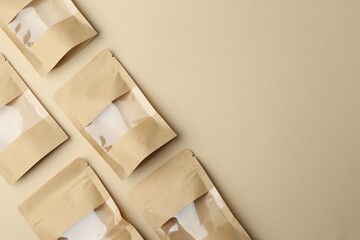 Many kraft stand-up pouches on beige background, flat lay. Space for text