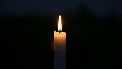 Single white candle glowing softly in darkness, solemn remembrance atmosphere.