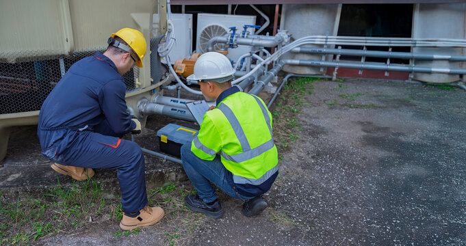 Two professional engineers inspecting industrial air conditioning system outside. Construction workers checking hvac maintenance with clipboard and toolbox at manufacturing factory site plant. - Powered by Adobe