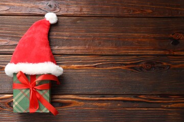 Christmas gift with Santa hat on wooden table, top view. Space for text