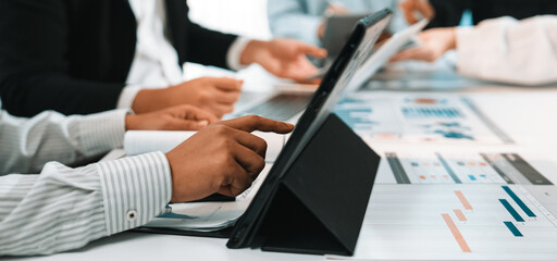 A group of professionals engage in a collaborative business meeting, analyzing data and developing strategies using laptops and documents on a bright office table. SACTR