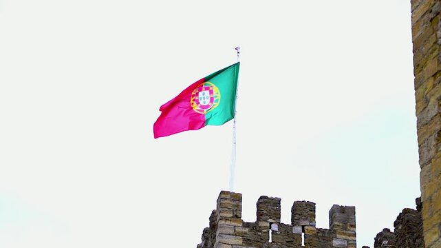The national flag of Portugal waving on top of a stone wall.