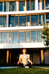 Young woman sitting on a grass against office building in lotus position