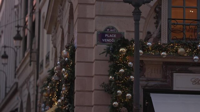 Establishing shot of Place Vendome street sign in Paris France decorated for Christmas with ornaments and lights Exterior view of building at dusk.