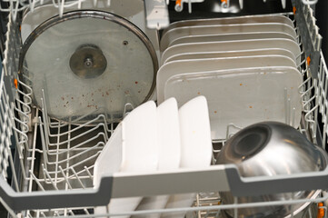Dirty dishes inside an open dishwasher. Plates, lid and bowls before washing, everyday household chores, hygiene, cleaning and modern kitchen interior.