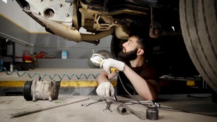 Auto mechanic examining car undercarriage with a work light, performing vehicle service and inspection at the garage. Truck repair service