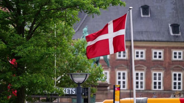 Denmark flag Dannebrog waving against a building and green tree in Copenhagen