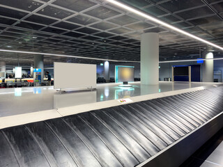 Baggage claim hall with empty luggage belt, bright lighting, modern columns and clearly structured ceiling design