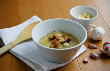 Traditional czech and slovak garlic soup cesnecka in white bowl with croutons and cheese on wooden table, homemade healthy vegetarian food, closeup rustic meal