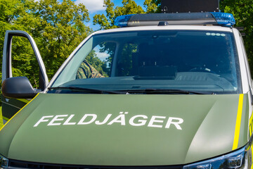 Front view of a Feldj&auml;ger vehicle with open door, blue light, uniform parts, green park background. Training, team, realistic exercises