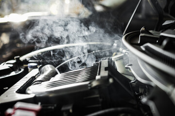  close-up of a car engine that has overheated, with smoke billowing from the engine compartment and causing damage.