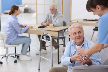 Care worker giving glass of water to senior woman at retirement home