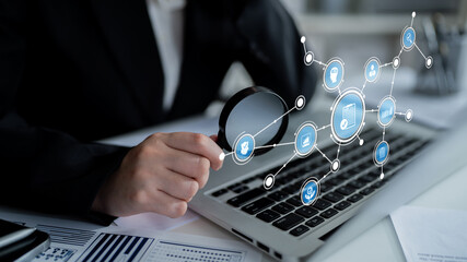 A business professional analyzes digital icons displayed on a laptop using a magnifying glass, emphasizing the intersection of technology and data analysis in a modern office setting. Tessel