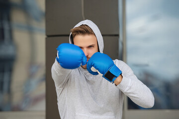 Strong boxer in sportswear. Exercising and punching. Practicing boxing. Sportsman in boxing gloves outdoor. Young man boxer. Sport man boxing. Strong athlete man. Sportsman in hoodie. Ring movement