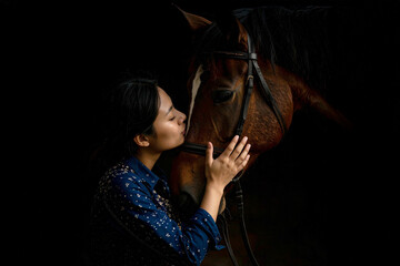 Dark, emotional portrait of a young female farmer gently hugging the head of her beloved horse, expressing trust, affection, and a deep bond between human and animal.