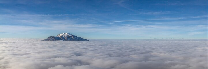 Solitary mountain peak rising above distant cloud sea