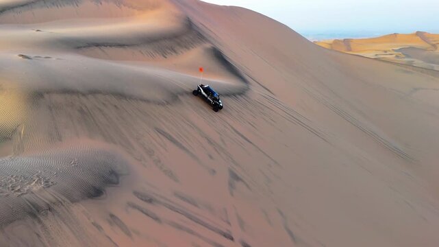 Aerial drone view of a buggy moving across the desert landscape in the Huacachina oasis at sunset, Peru.	