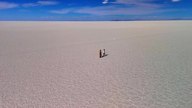 Aerial drone video of a man and woman in Salar de Uyuni, Bolivia. The couple walks across the vast salt flat, enjoying the surrounding landscape. 