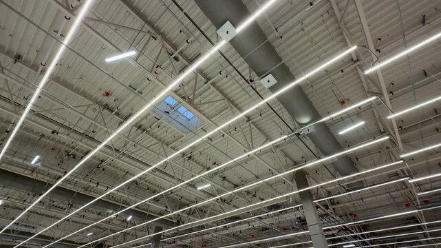 Industrial Warehouse Ceiling With Skylight Panels Showcasing Grid Of LED Fixtures, Metal Rafters, Ventilation Ducts, And Maintenance Access Points Creating Bright Daylight Interior