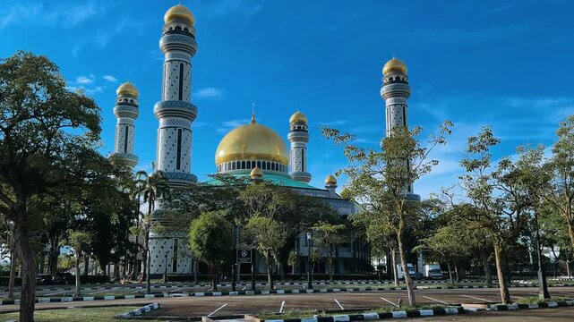 The golden dome and building of the Jamil Asra Hassan Al-Bolkiah Mosque in Bandar Seri Bagawan, Brunei Darussalam, are framed by tropical palm trees on a sunny day. Asia. 4К