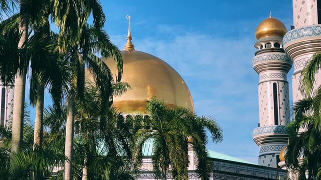 The golden dome and building of the Jamil Asra Hassan Al-Bolkiah Mosque in Bandar Seri Bagawan, Brunei Darussalam, are framed by tropical palm trees on a sunny day. Asia. 4К