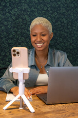 African American woman smiles at camera of her phone. female blogger records video or conducts live broadcast. happy young person is working on a laptop.