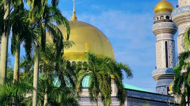 The golden dome and building of the Jamil Asra Hassan Al-Bolkiah Mosque in Bandar Seri Bagawan, Brunei Darussalam, are framed by tropical palm trees on a sunny day. Asia. 4К