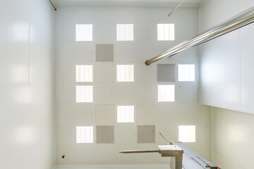 view straight up at cassette suspended ceiling with square fluorescent lights or halogen spots lamps  in a work area or hallway with ventilation