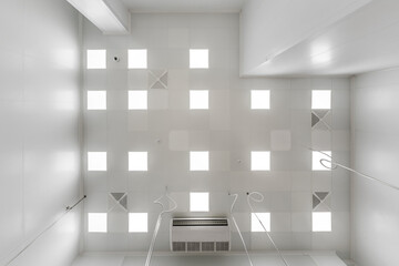 view straight up at cassette suspended ceiling with square fluorescent lights or halogen spots lamps  in a work area or hallway with ventilation