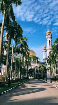 The golden dome and building of the Jamil Asra Hassan Al-Bolkiah Mosque in Bandar Seri Bagawan, Brunei Darussalam, are framed by tropical palm trees on a sunny day. Asia. 4К
